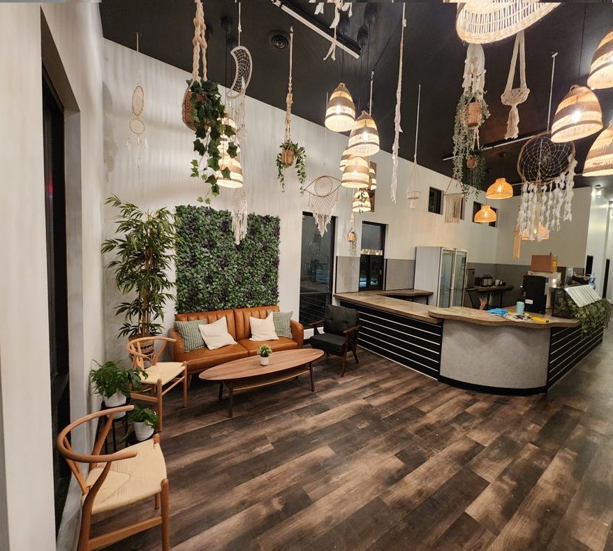 Coffee shop after: wood-look floors, plant wall, leather sofa, pendant lights over a long counter